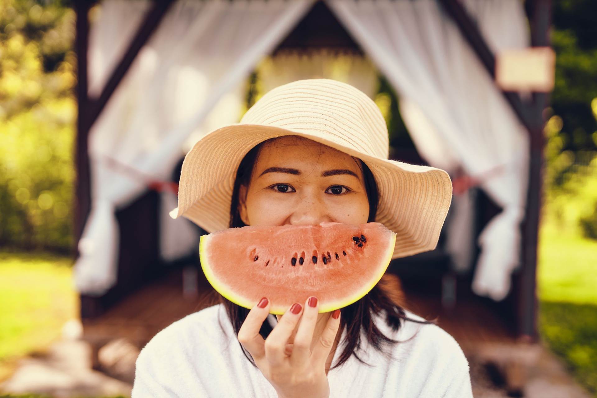 Frau mit Hut hält Melonenspalte vor ihr Gesicht
