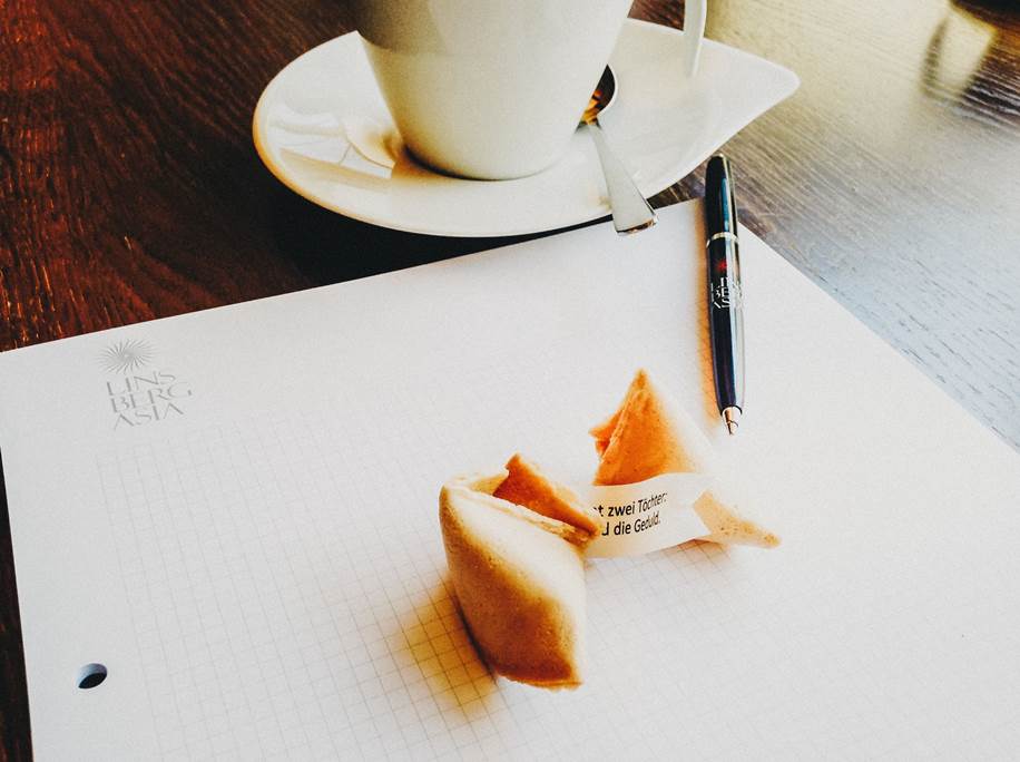 Fortune cookie on notepad and cup of coffee