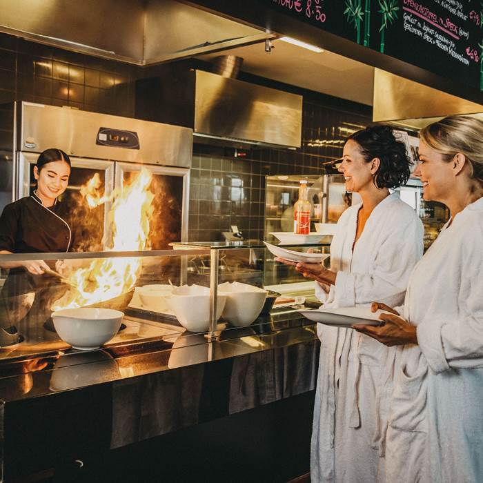 Two women in bathrobe watch cook cooking