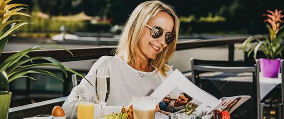 Genießen Sie einen entspannten Thermentag nur für sich Frau frühstückt auf Terrasse und liest eine Zeitschrift