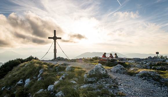 Die malerische Wanderregion lockt mit spannenden Ausflugszielen und beeindruckenden Aussichten Wanderer rasten bei Gipfelkreuz